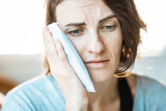 woman in pain holds icepack to side of face